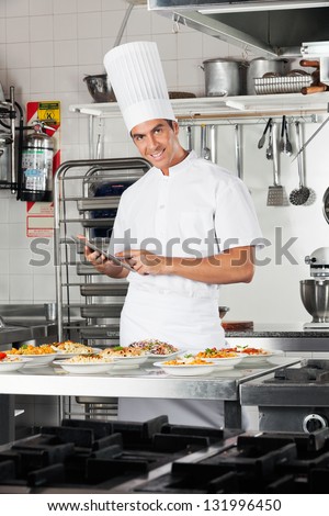 Portrait of happy male chef with digital tablet checking list of pastas at commercial kitchen counter