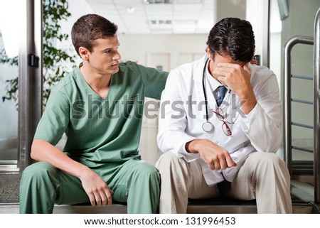Young male colleague in uniform comforting an upset doctor