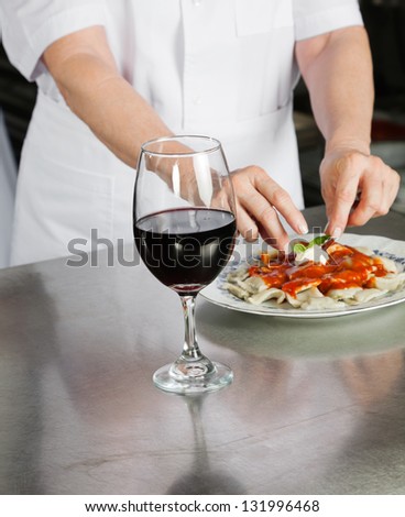 Midsection of male chef garnishing pasta dish with wine glass on kitchen counter