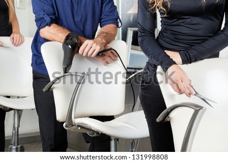 Midsection of hairdressers with dryer and scissors standing behind chairs in salon