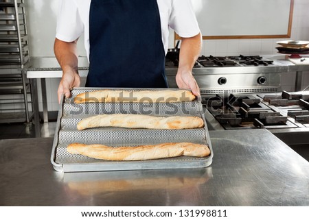 Midsection of male chef presenting bread loafs in industrial kitchen