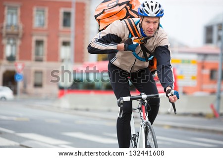 Young male cyclist with courier delivery bag riding bicycle on street