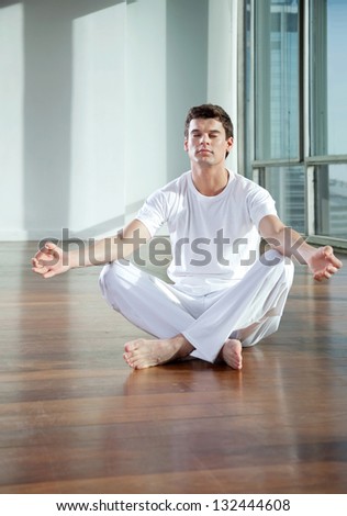 Full length of a young man practicing yoga in lotus position at gym