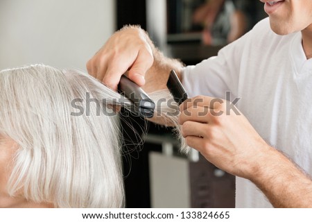 Closeup of hairstylist's hands straightening hair of female client in salon