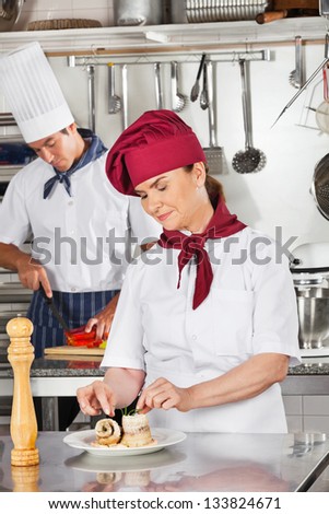 Female chef garnishing dish with male colleague in background