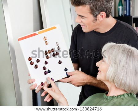Senior woman with male hair stylist selecting hair color from catalog at salon