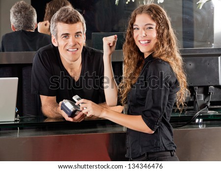 Portrait of happy young woman paying with mobilephone over electronic reader and hairdresser at salon counter