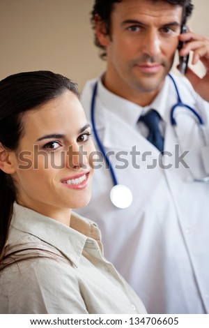 Portrait of beautiful woman smiling while doctor answering phone call in background