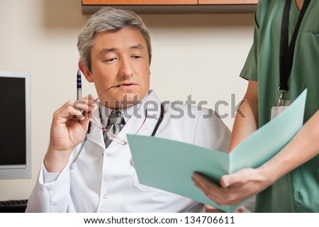 Midsection of male technician showing patient's file to mature doctor