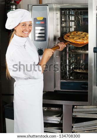 Portrait of mid adult female chef placing pizza in oven at commercial kitchen