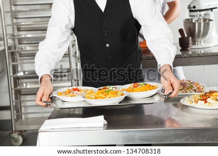Midsection of waiter holding pasta dishes in tray at restaurant kitchen