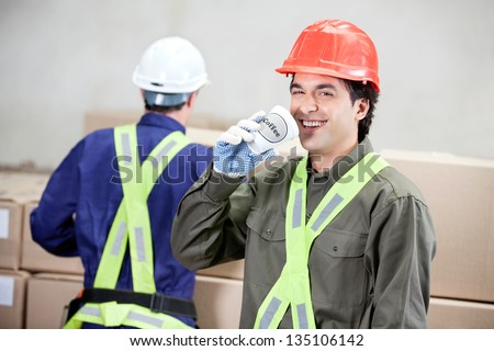 Portrait of young foreman drinking coffee while colleague working at warehouse