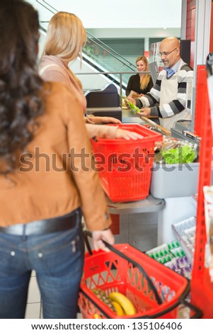 Customers with shopping baskets standing in line at checkout counter in supermarket