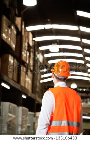 Rear view of male supervisor wearing protective vest and helmet at warehouse