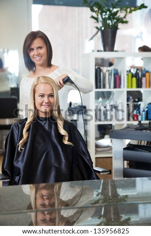 Mirror reflection of stylist curling hair of young woman at parlor
