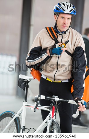 Young male cyclist in protective gear with courier bag using walkie-talkie