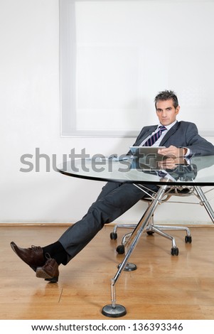 Portrait of relaxed mid adult businessman using digital tablet at desk in office
