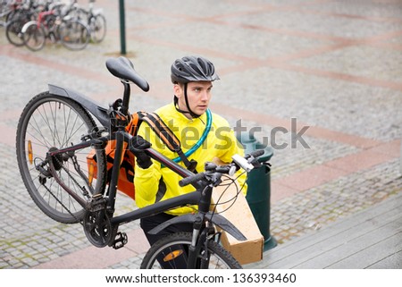 Young male cyclist with courier bag and bicycle walking up steps