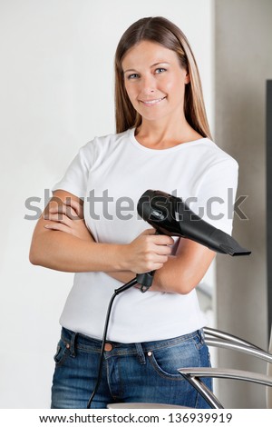 Portrait of confident female hairstylist with hairdryer in beauty parlor