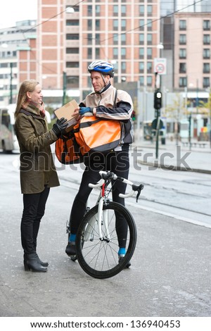 Young woman receiving a package from courier delivery man with bicycle and backpack