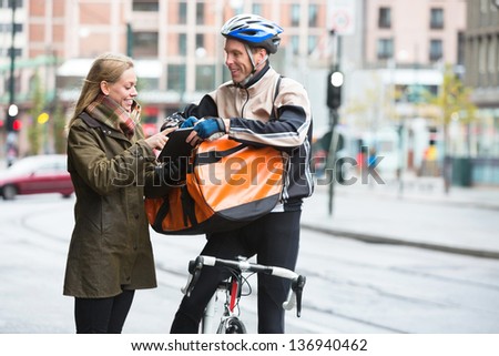 Courier delivery man with backpack showing digital tablet to young woman on street