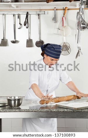 Happy female chef rolling dough on kitchen counter