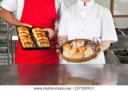 Midsection of chefs holding baked breads in industrial kitchen