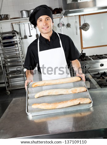 Portrait of young male chef showing baked bread loafs in industrial kitchen