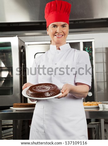 Portrait of female chef presenting chocolate cake in industrial kitchen