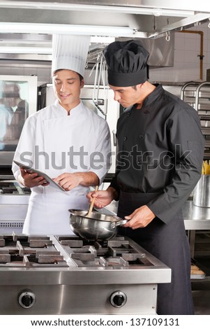 Young male chefs with digital tablet preparing food in restaurant kitchen