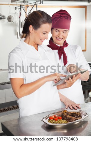 Happy female chefs looking for recipe on a digital tablet while cooking at kitchen
