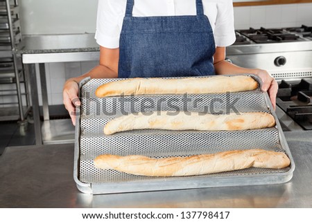 Midsection of female chef presenting baked loafs in restaurant kitchen