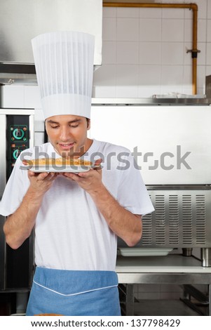 Young male chef smelling sweet dish in commercial kitchen