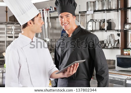 Portrait of male chef with colleague holding digital tablet in commercial kitchen