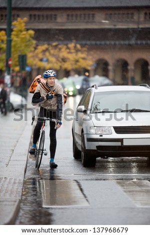Young male cyclist in protective gear with backpack using walkie-talkie on street