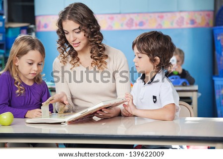 Little children and teacher reading book at desk in preschool