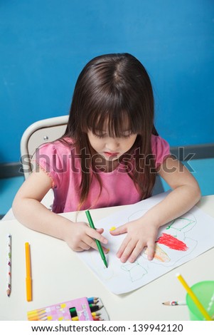 Cute preschool girl drawing with sketch pen at desk in classroom