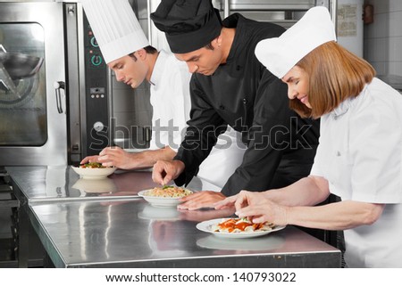 Three chefs garnishing dishes on commercial kitchen counter