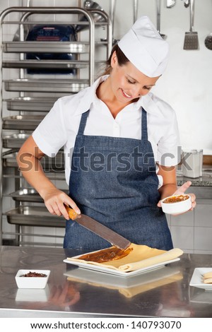 Happy female chef preparing chocolate roll in industrial kitchen