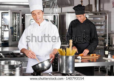 Happy male chefs preparing food in industrial kitchen