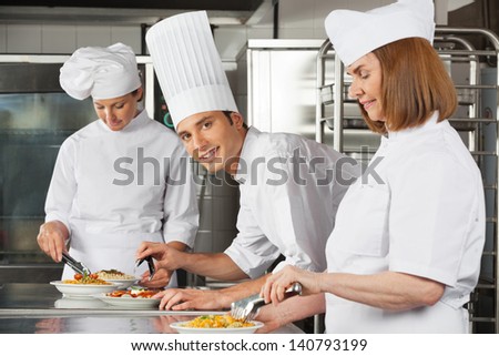 Portrait of young male chef with female colleagues working in industrial kitchen