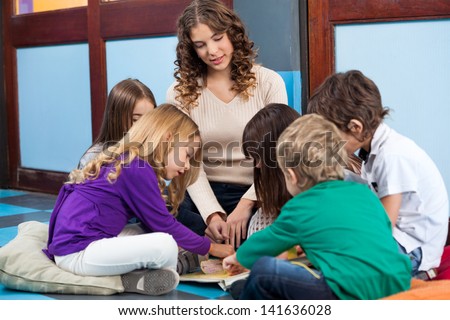 Teacher and students reading book on floor in preschool