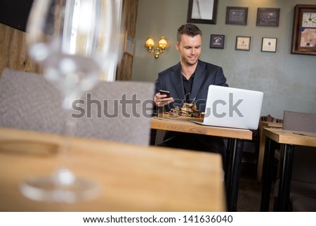 Young business man with laptop and mobilephone having meal in restaurant