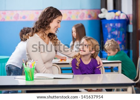 Little girl looking at kindergarten teacher with students in background