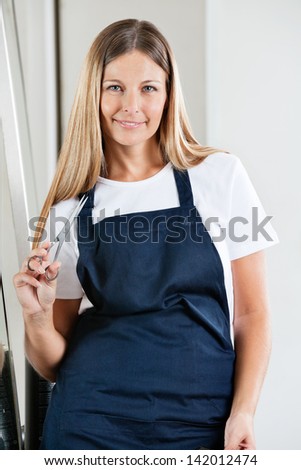 Portrait of mid adult female hairdresser holding scissors in beauty parlor
