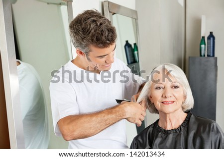 Senior client getting haircut by male hairstylist at salon