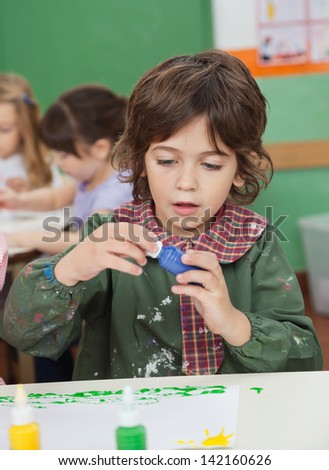 Cute little boy looking at watercolor while classmates painting in background