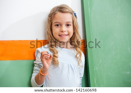 Portrait of cute little girl standing by green chalkboard in classroom