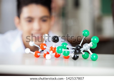 Molecular structure on desk with teenage boy looking at it in lab