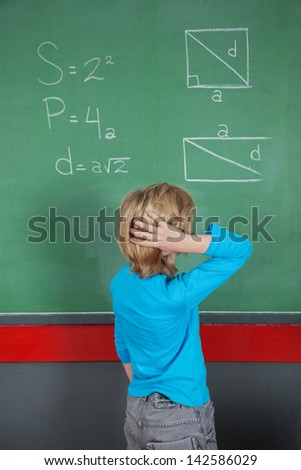 Rear view of confused little boy looking at board in classroom
